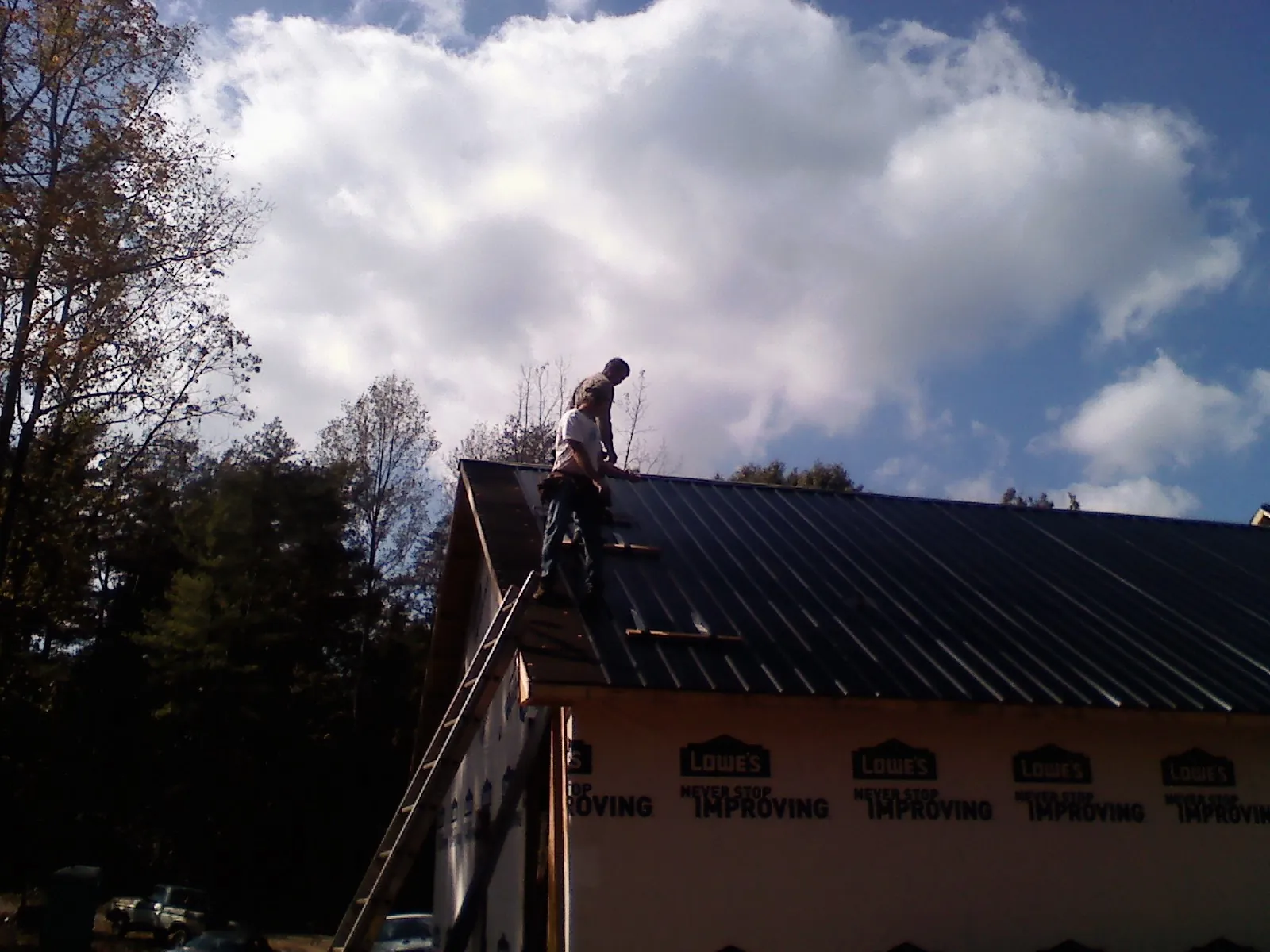 Roofer fastening dark metal panels high against a cloudy sky, from a Roof Inspection job in Stanley