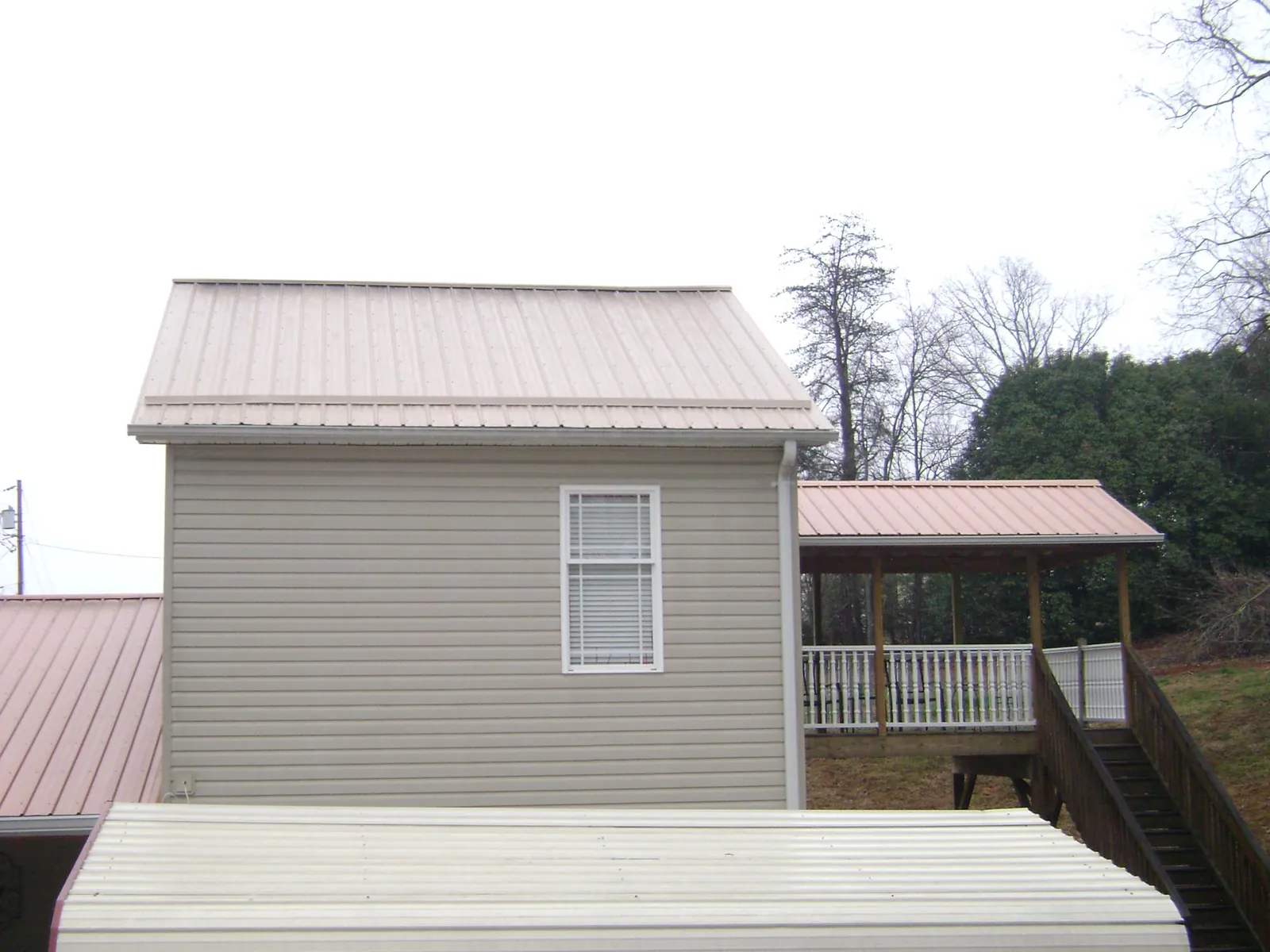 Tan metal roofs on a two story addition and attached porch, from a Roof Replacement job in Stanley